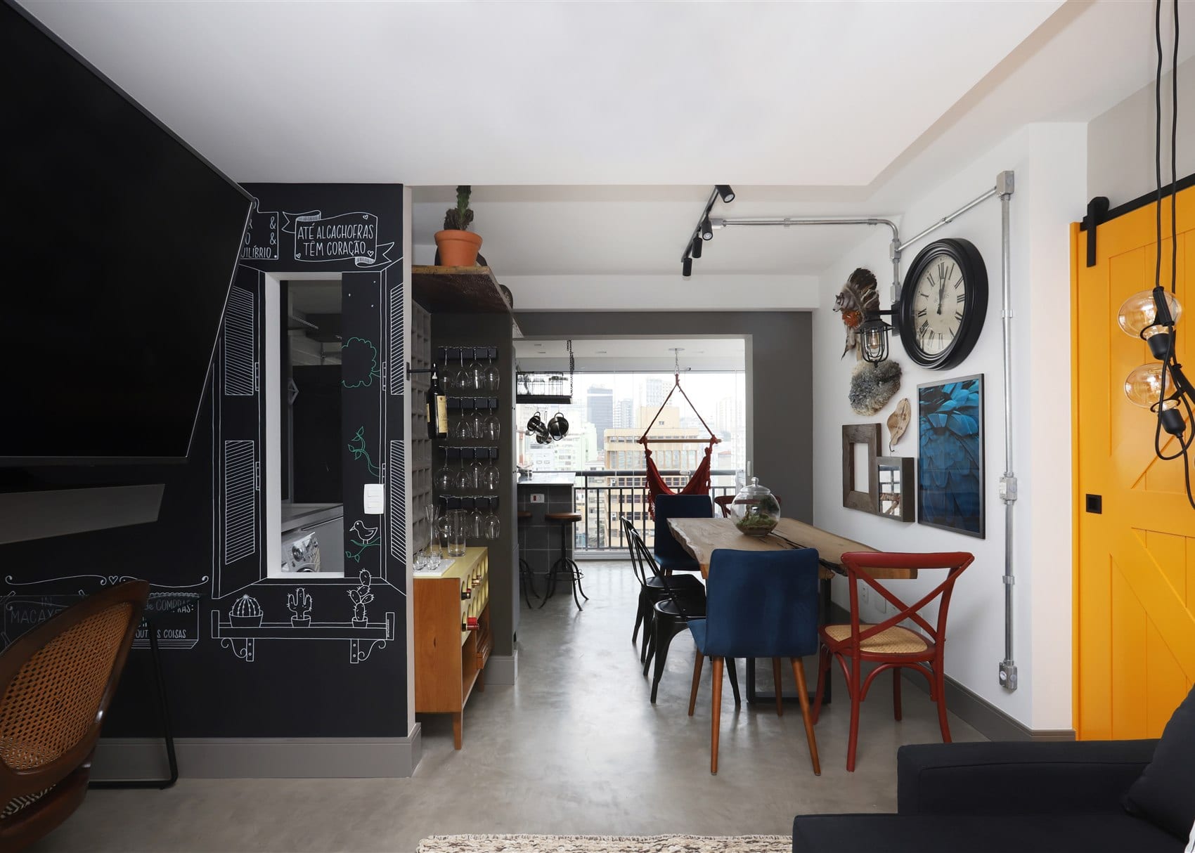 Bela Vista: a sala social completa com lousa, mesa de demolicao, rede vermelha na varanda e a porta amarela ao fundo, foto Mariana Orsi