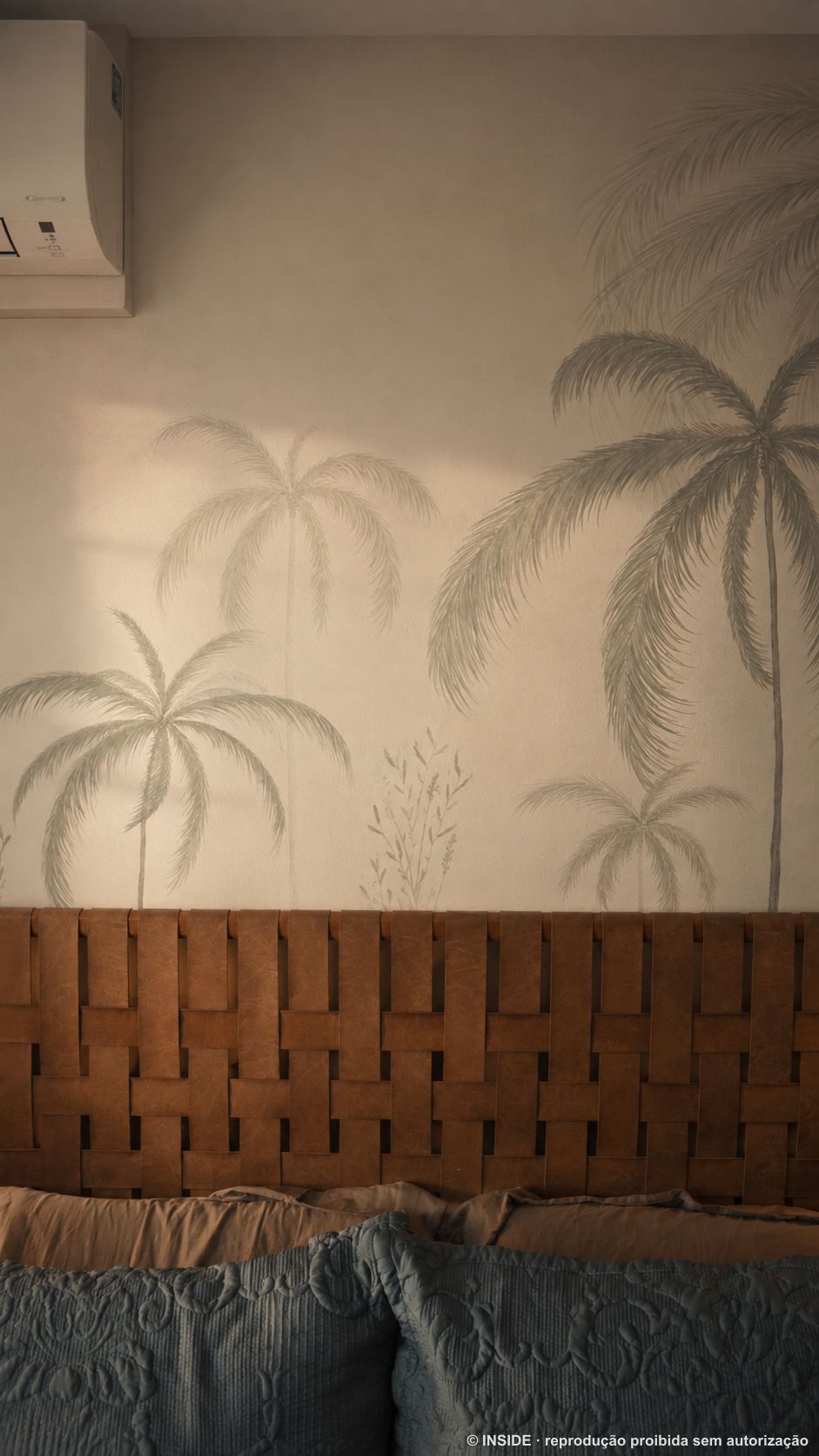 Cabeceira de couro trançado caramelo sob mural de palmeiras pintado em tons suaves, projeto INSIDE