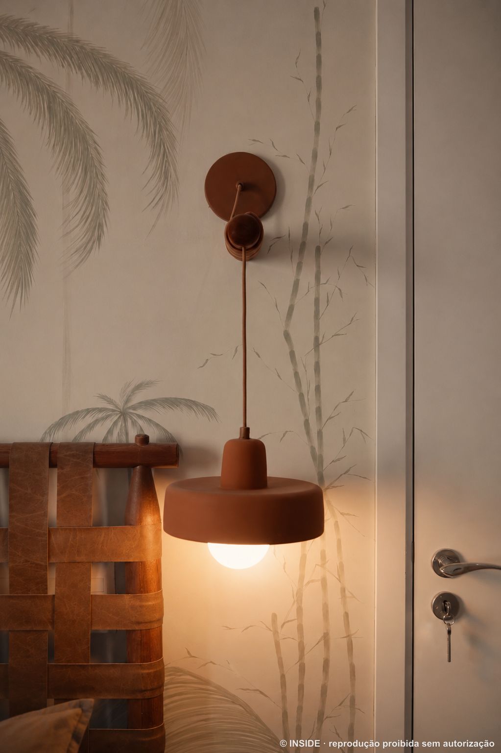 Detalhe da luminária de terracota com globo aceso e suporte de madeira torneada na parede do quarto, projeto INSIDE