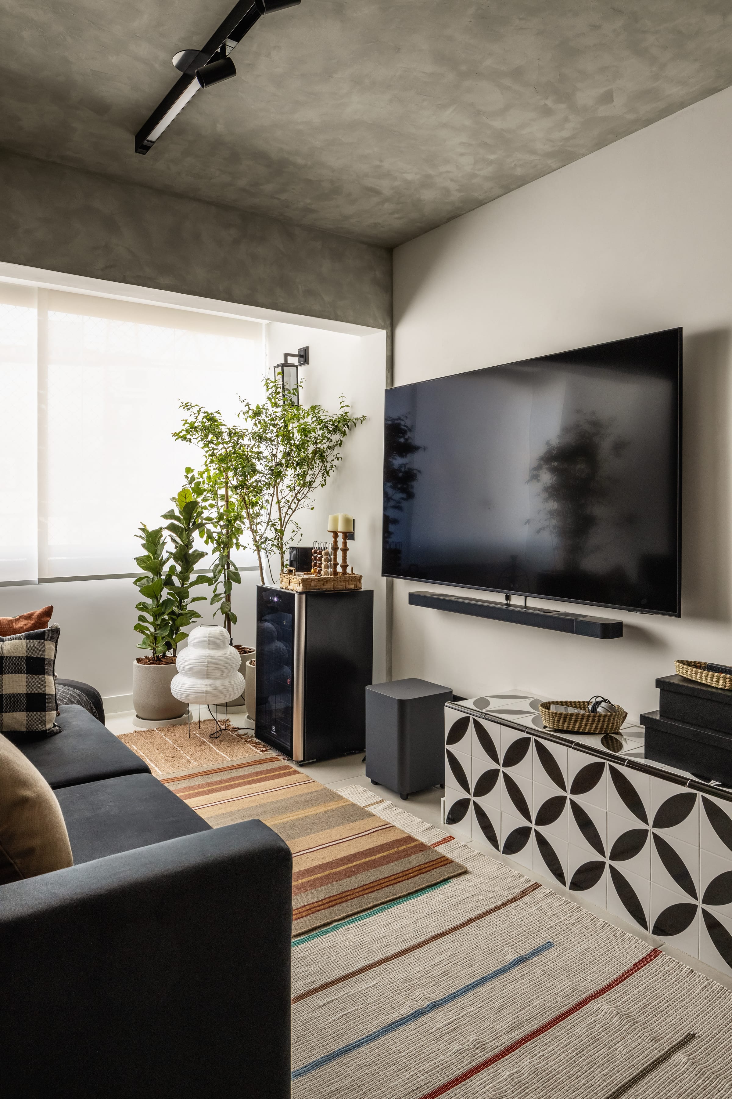 Estar com painel de TV, aparador de ladrilho geométrico preto e branco e kilim listrado, projeto INSIDE