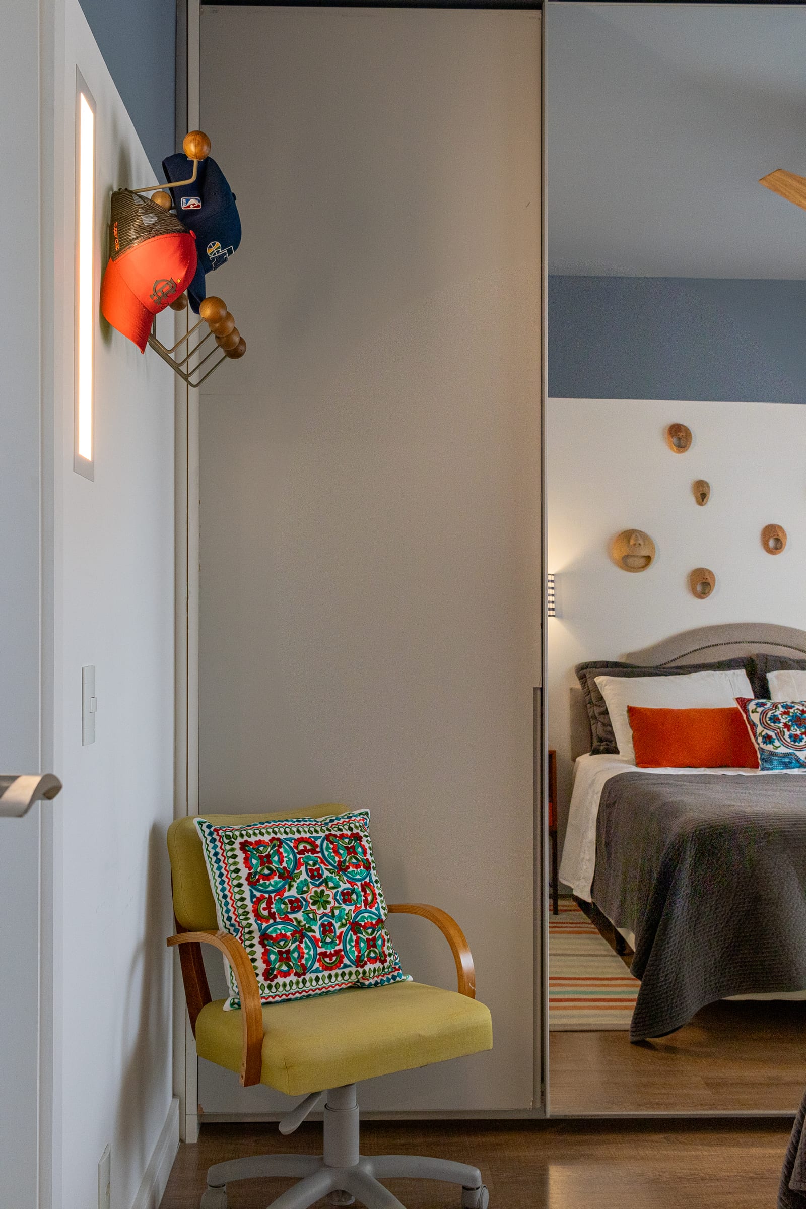 Quarto com cadeira giratória amarela vintage, closet de correr e cabeceira com máscaras de cerâmica ao fundo, projeto INSIDE