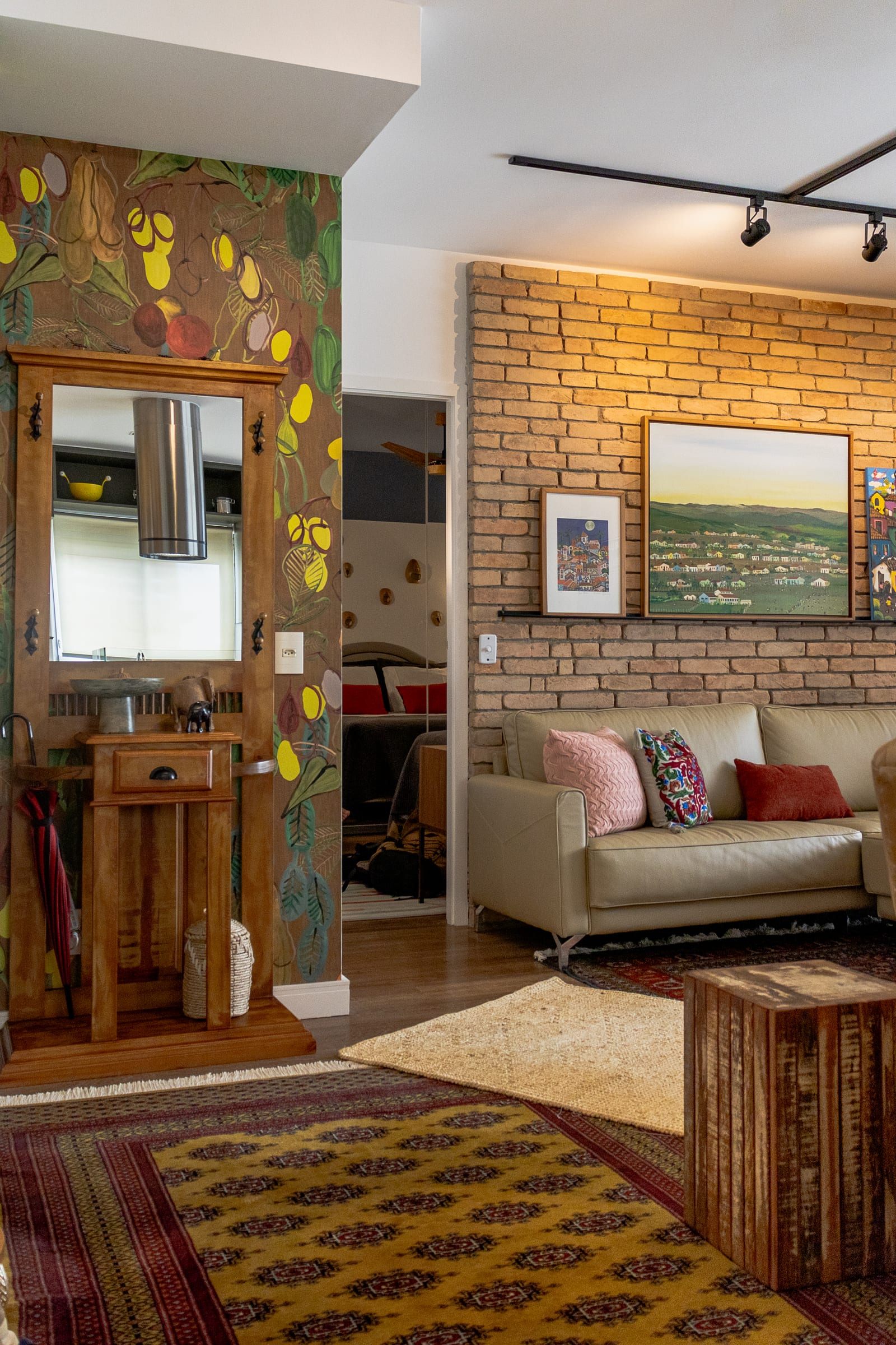 Entrada com papel de parede tropical de frutas, espelho de madeira e coifa cilíndrica ao fundo, ao lado da sala de tijolo, projeto INSIDE