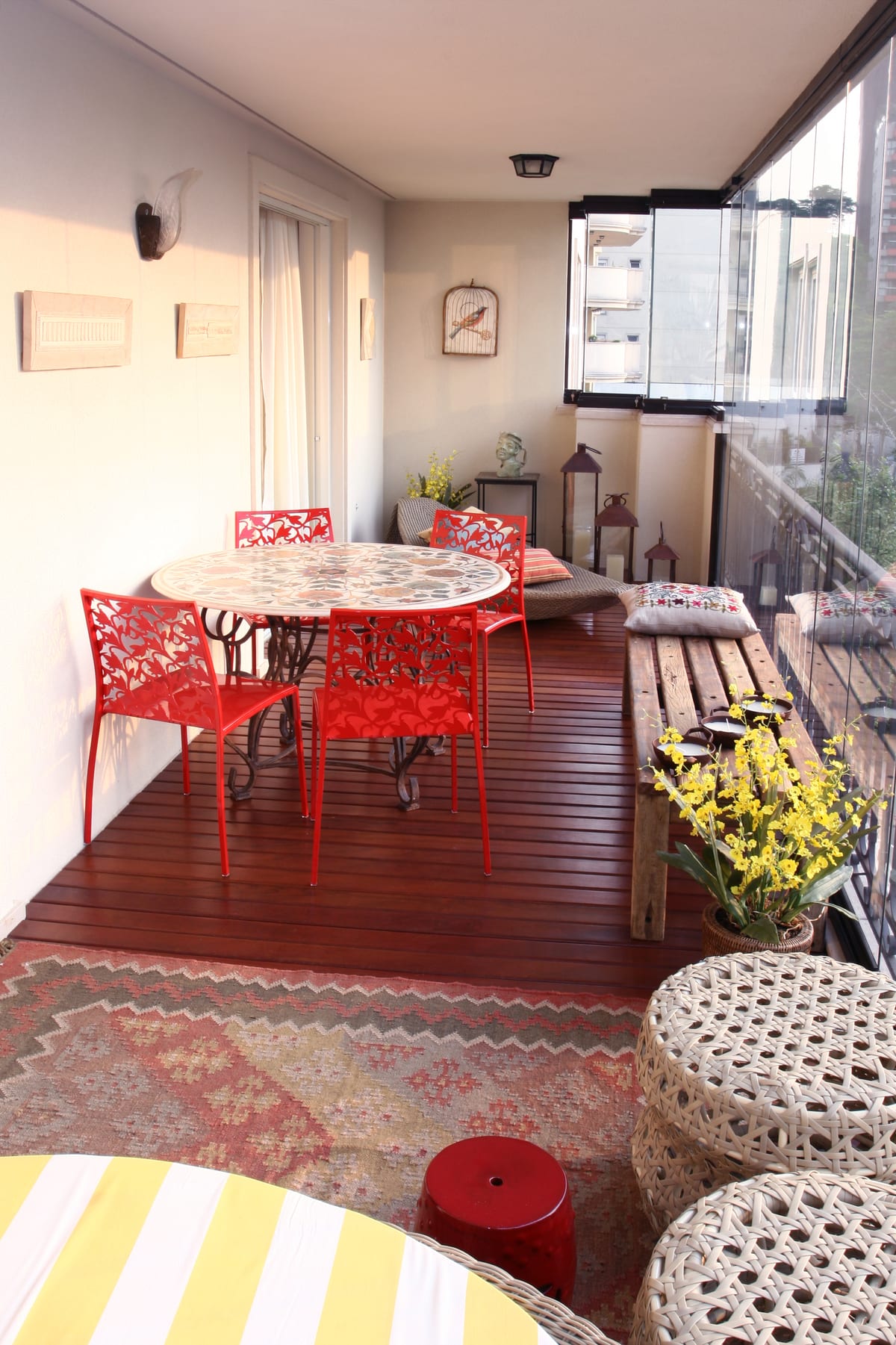 Rosa Albuquerque: a varanda envidraçada com deck de madeira, mesa de mosaico e cadeiras vermelhas, acervo INSIDE