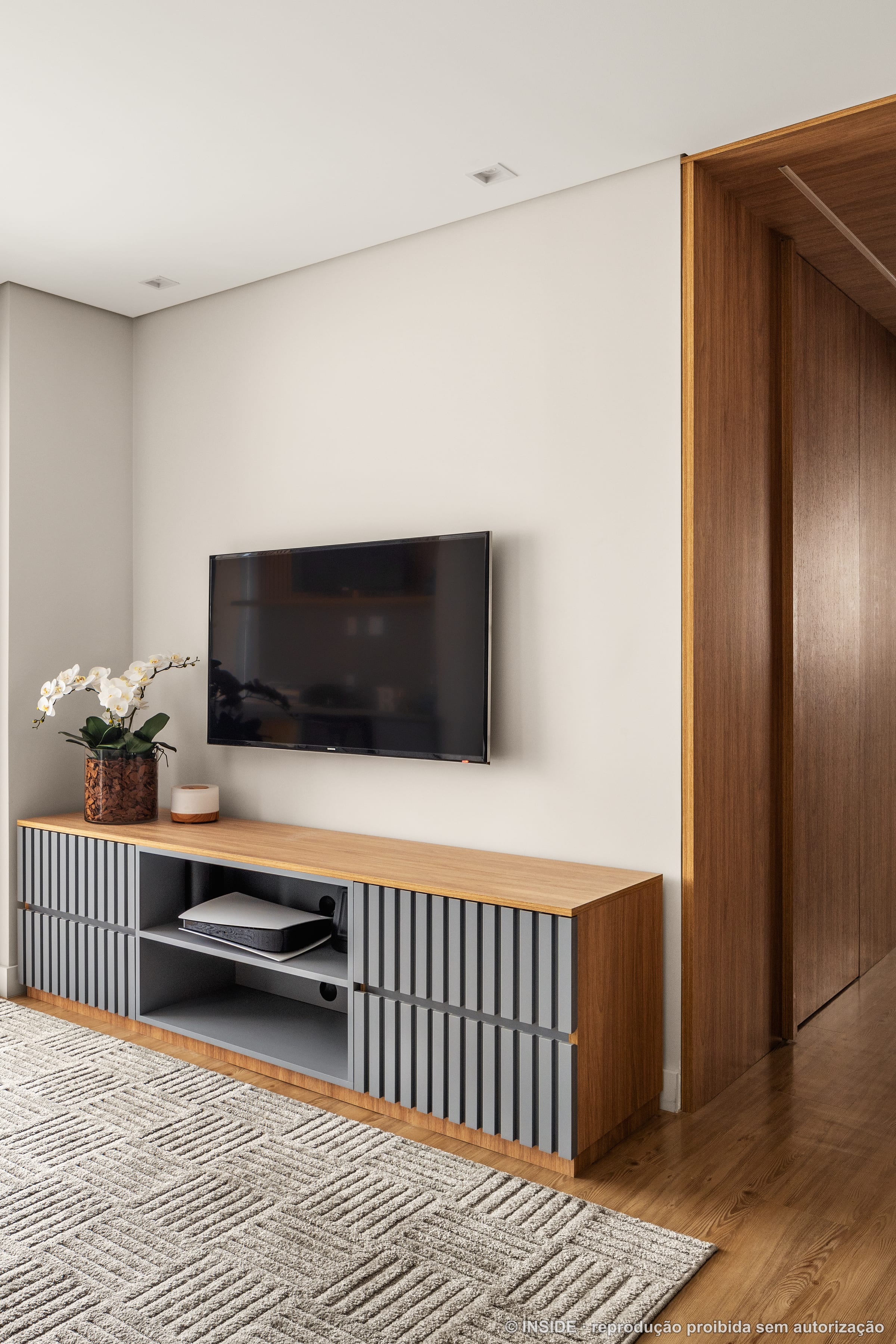Sala de estar com painel de madeira, televisão e rack ripado, vaso com flores, projeto INSIDE