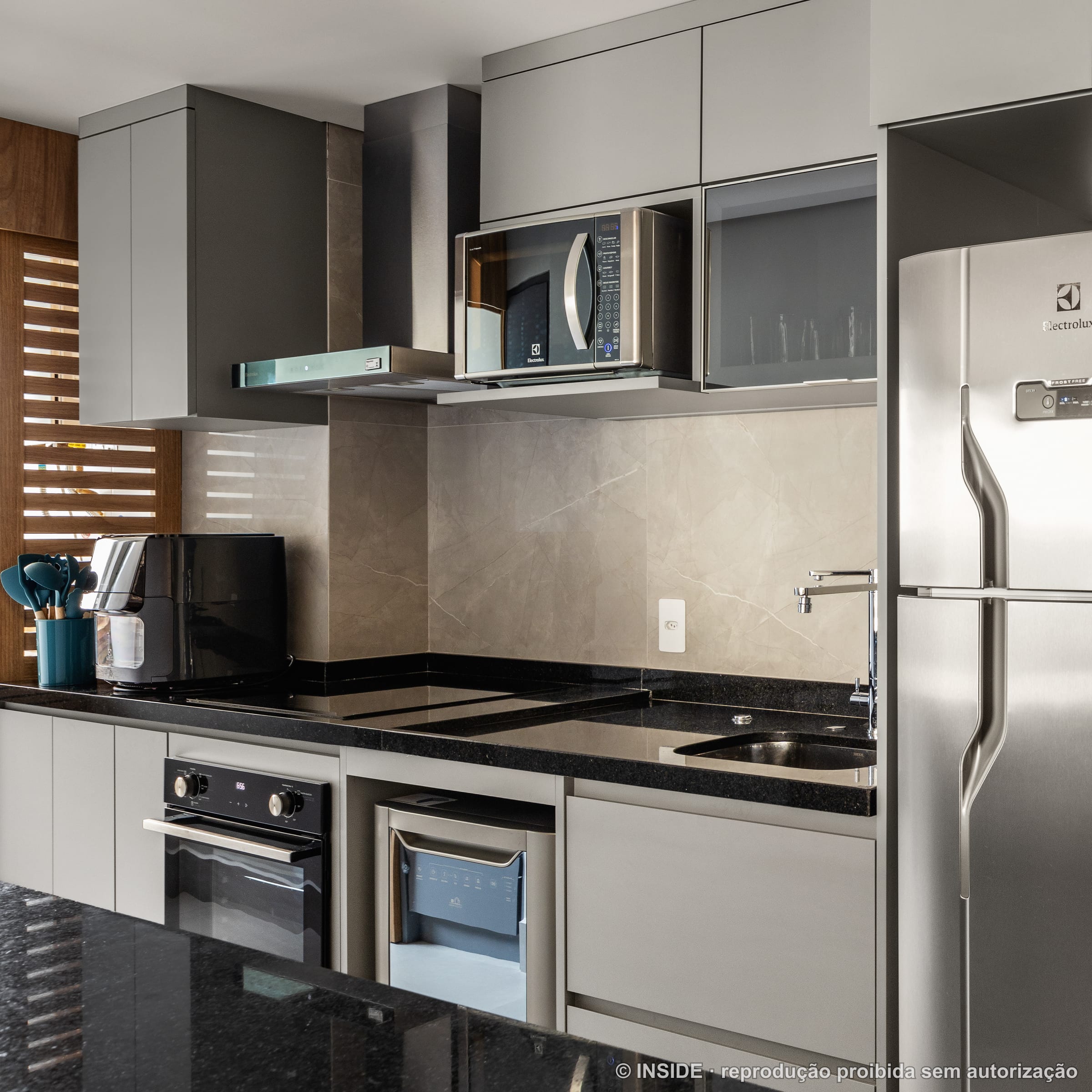 Cozinha compacta com bancada preta, cooktop, forno e geladeira, projeto INSIDE