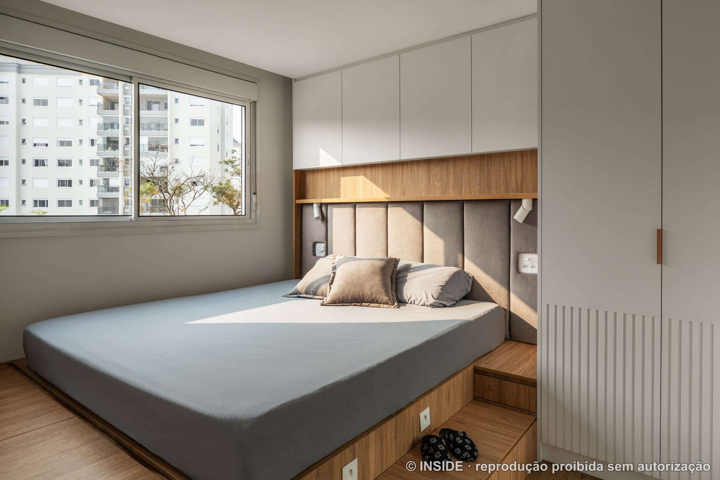 Quarto de casal com cabeceira em madeira ripada, roupa de cama clara e janela com vista, projeto INSIDE