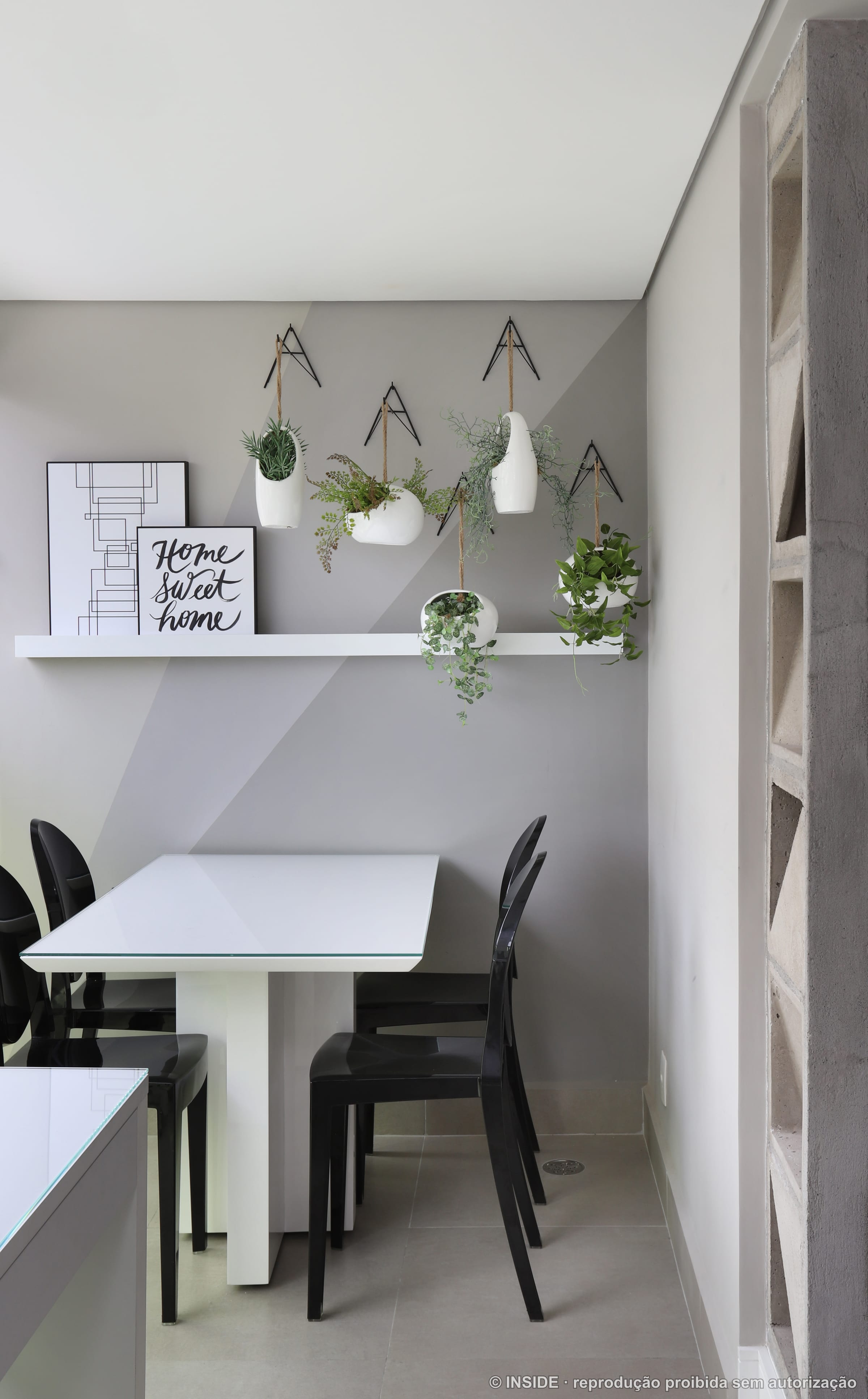 Área de jantar com mesa dobrável de parede, cadeiras pretas e prateleira com vasos de plantas suspensas, projeto INSIDE