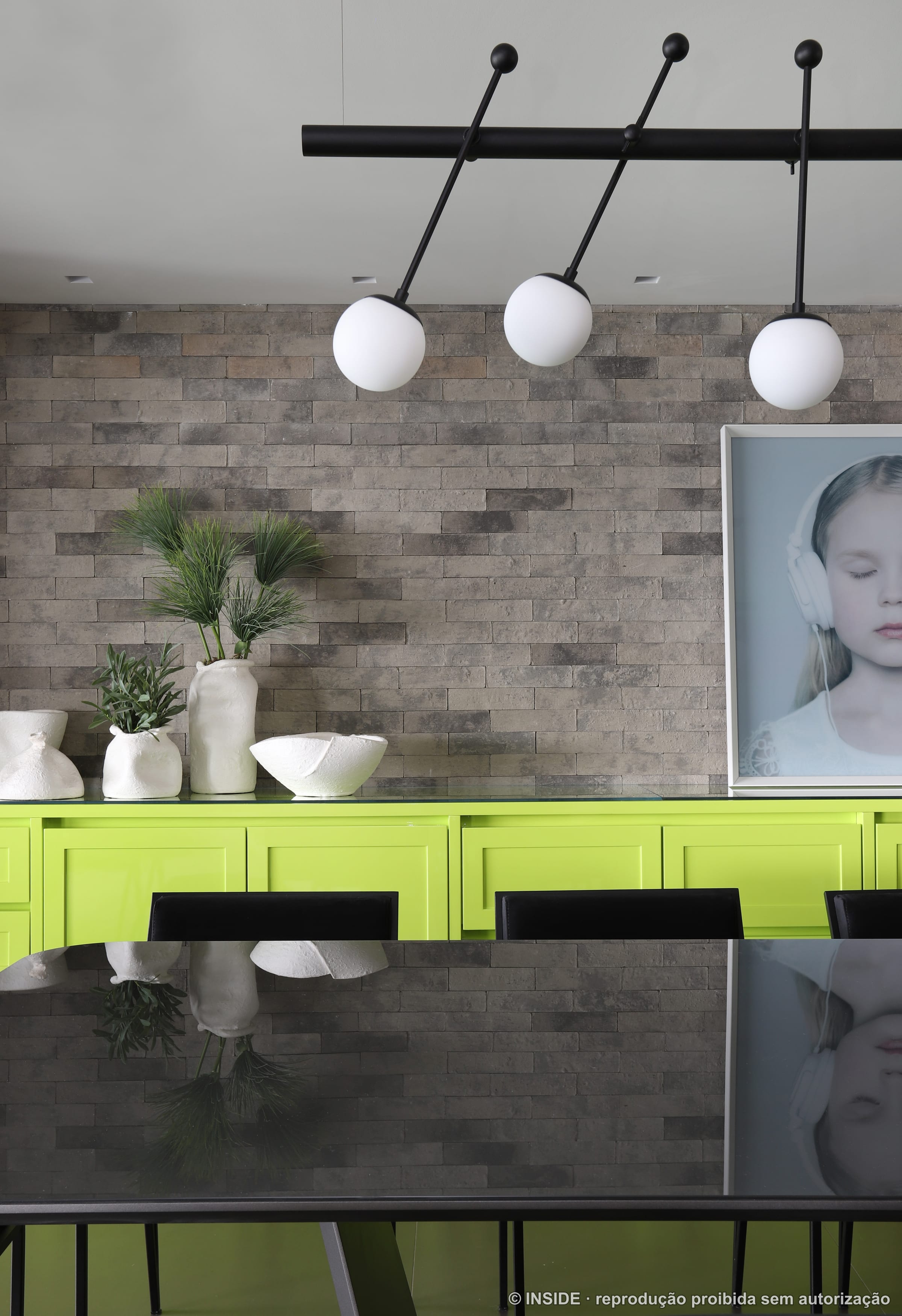 Sala de jantar com retrato de menina emoldurado, marcenaria verde-limão e parede de pedra, projeto INSIDE