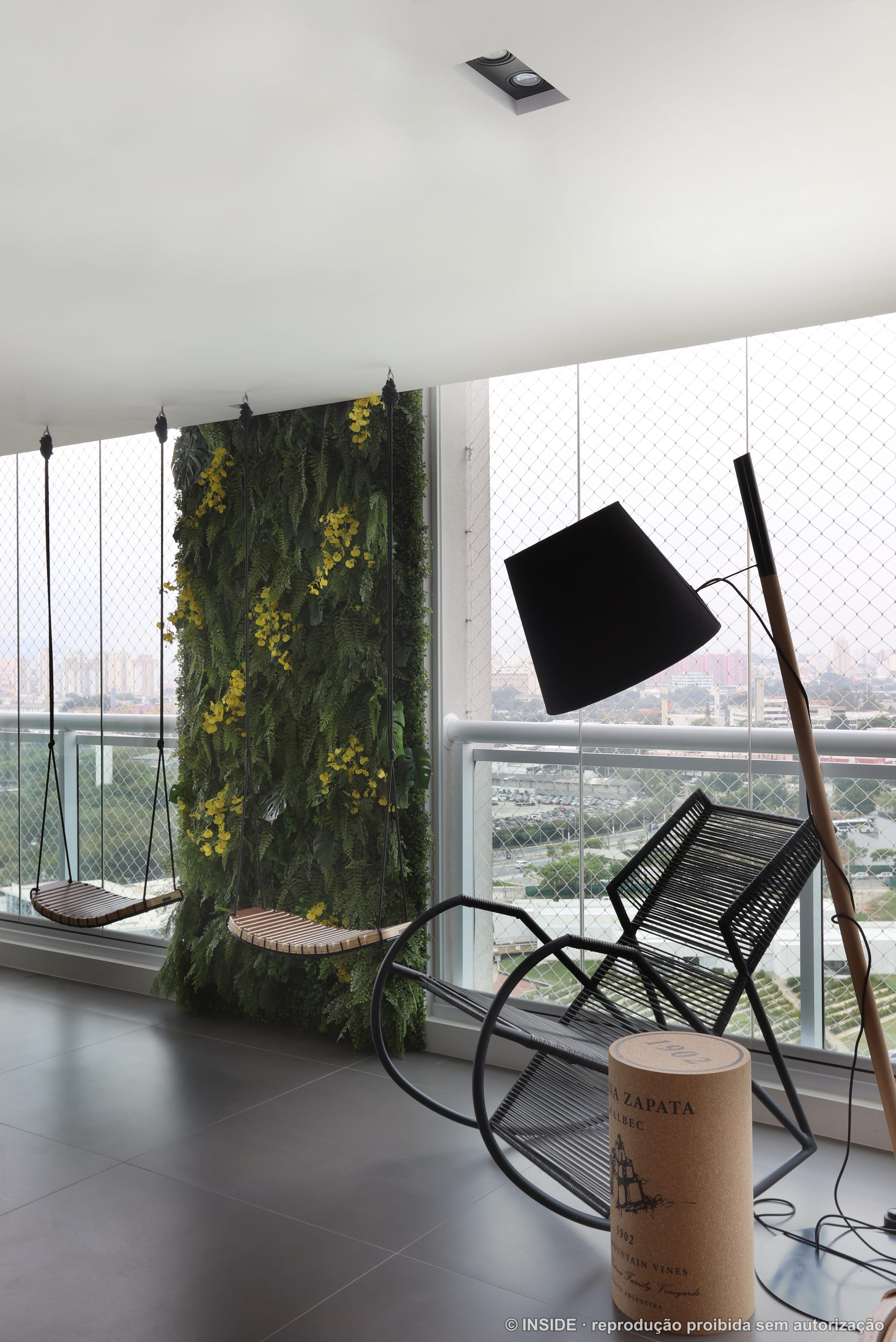 Terraço com jardim vertical florido, poltronas e luminária de piso, com a cidade ao fundo, projeto INSIDE