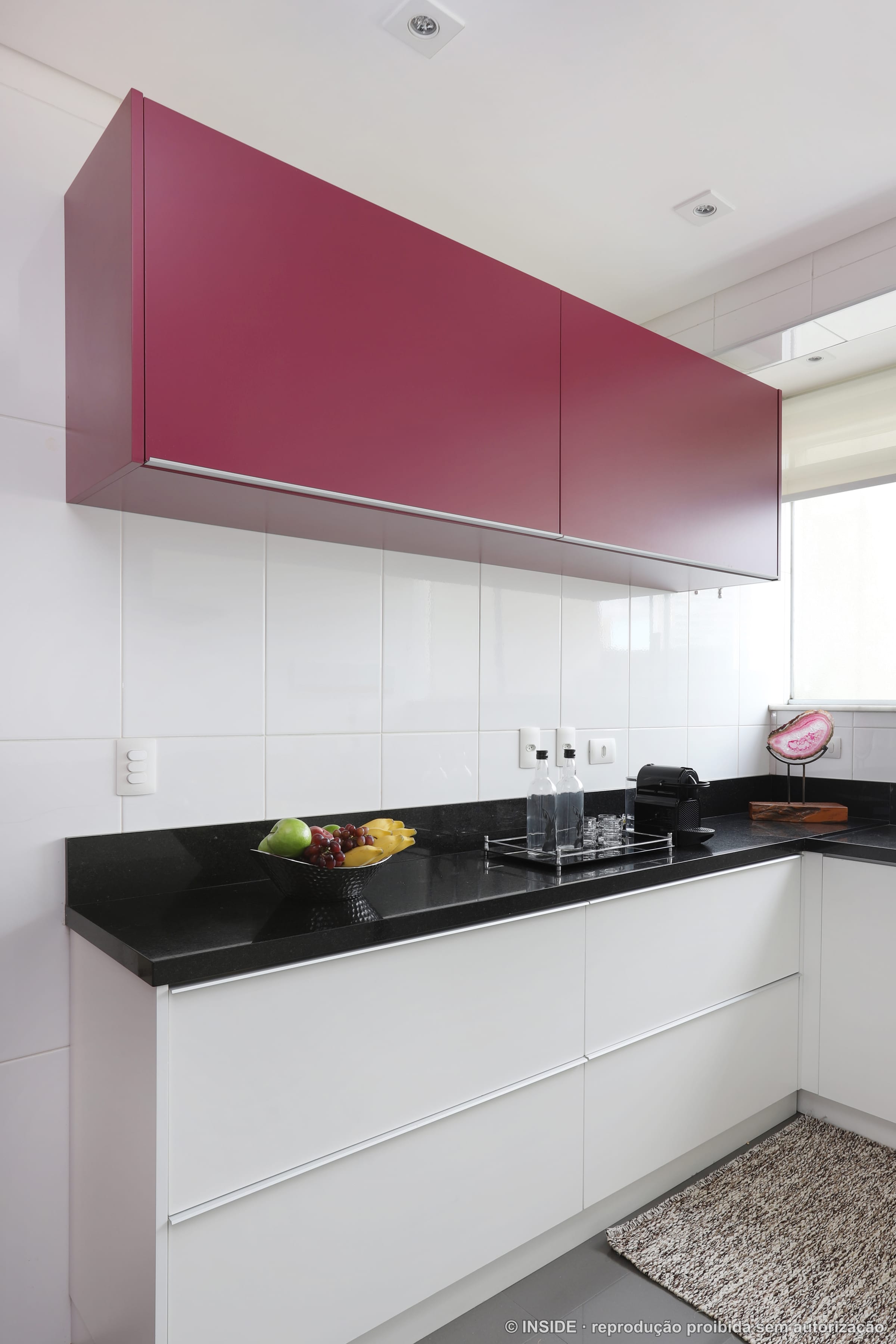 Cozinha com marcenaria branca, bancada preta e um módulo em magenta, projeto INSIDE