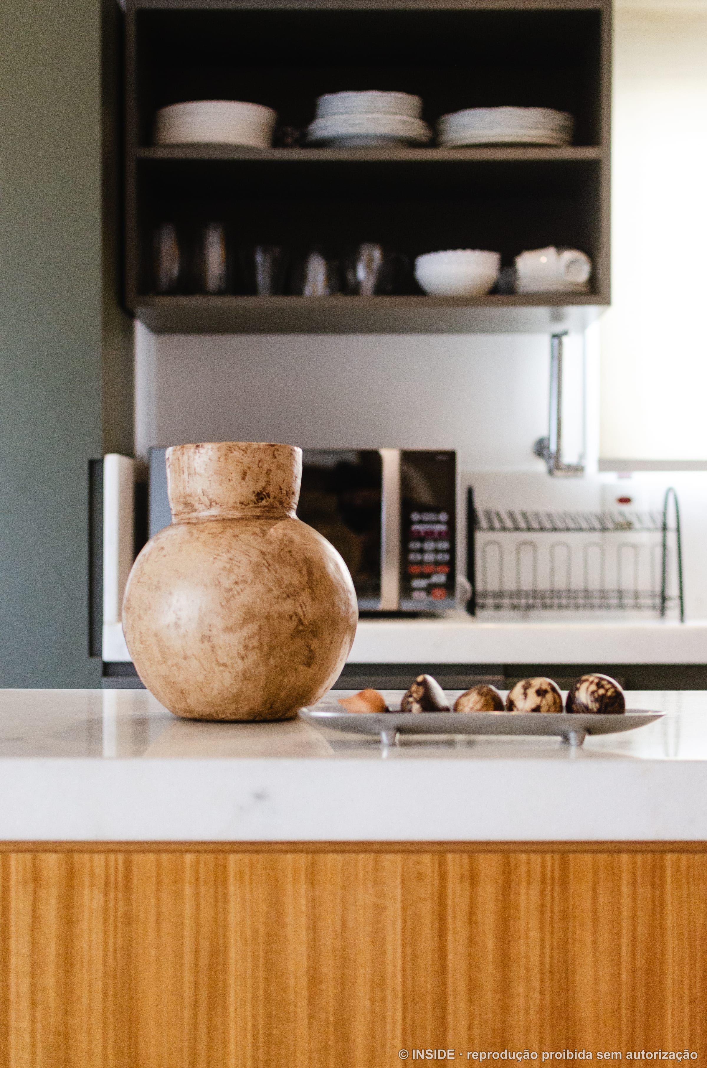 Detalhe de bancada com vaso artesanal em terracota e vista para cozinha com prateleiras abertas ao fundo, projeto INSIDE