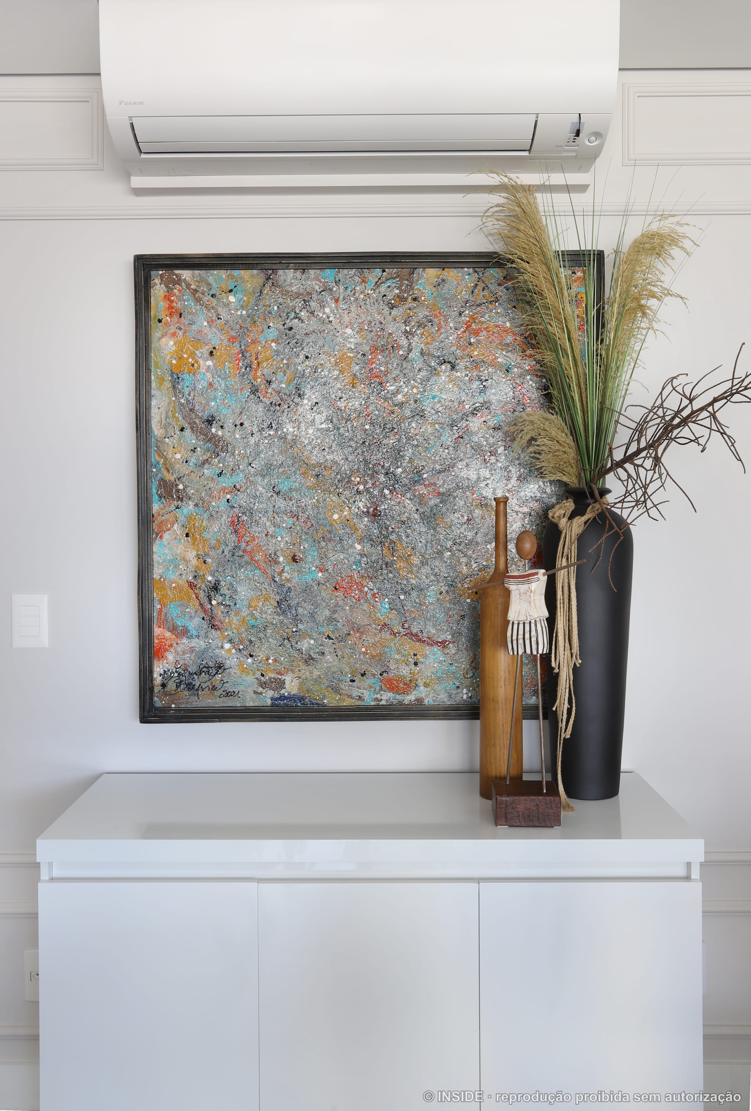 Painel de arte abstrata colorida na parede com vaso alto e galhos secos, projeto INSIDE