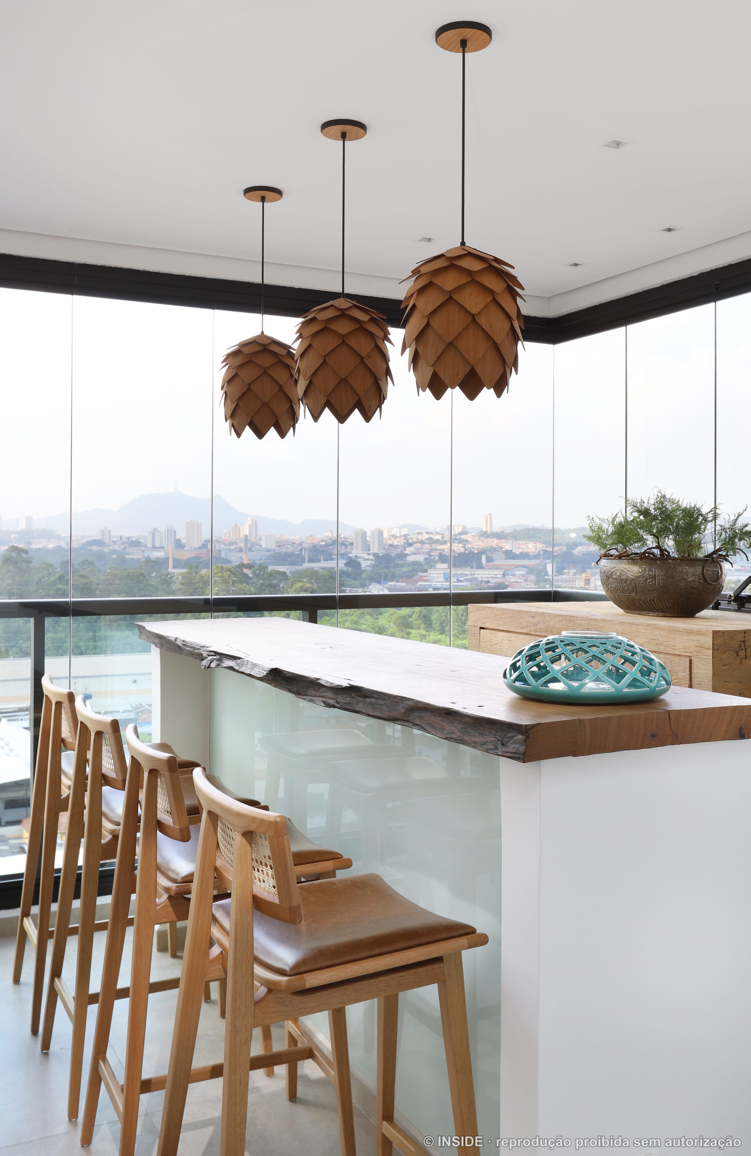 Bar da varanda gourmet com bancada de madeira, banquetas e a cidade ao fundo, projeto INSIDE