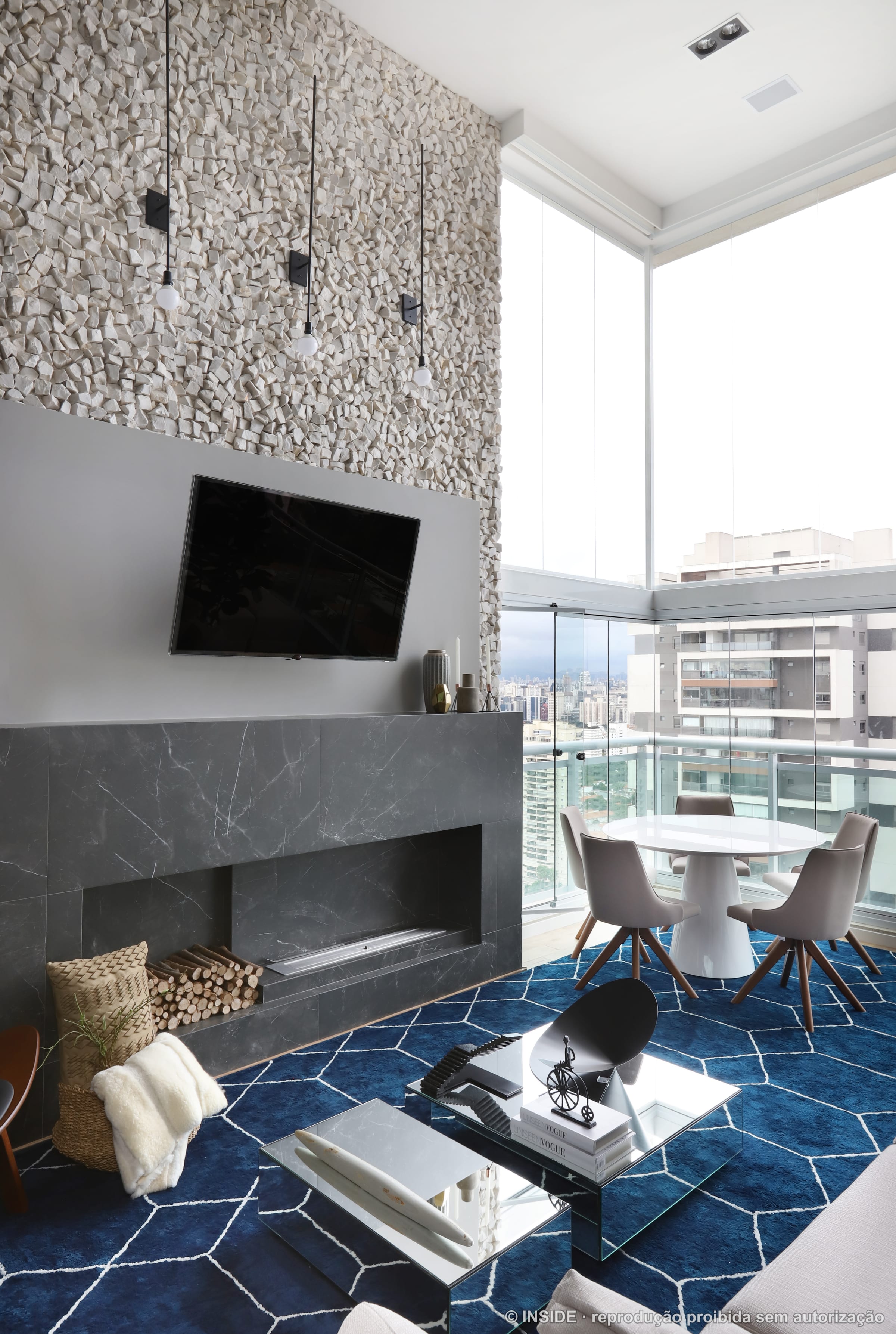 Canto de estar com painel de TV em mármore escuro, lareira, mesa de centro em vidro e portas de vidro para a varanda com vista, projeto INSIDE