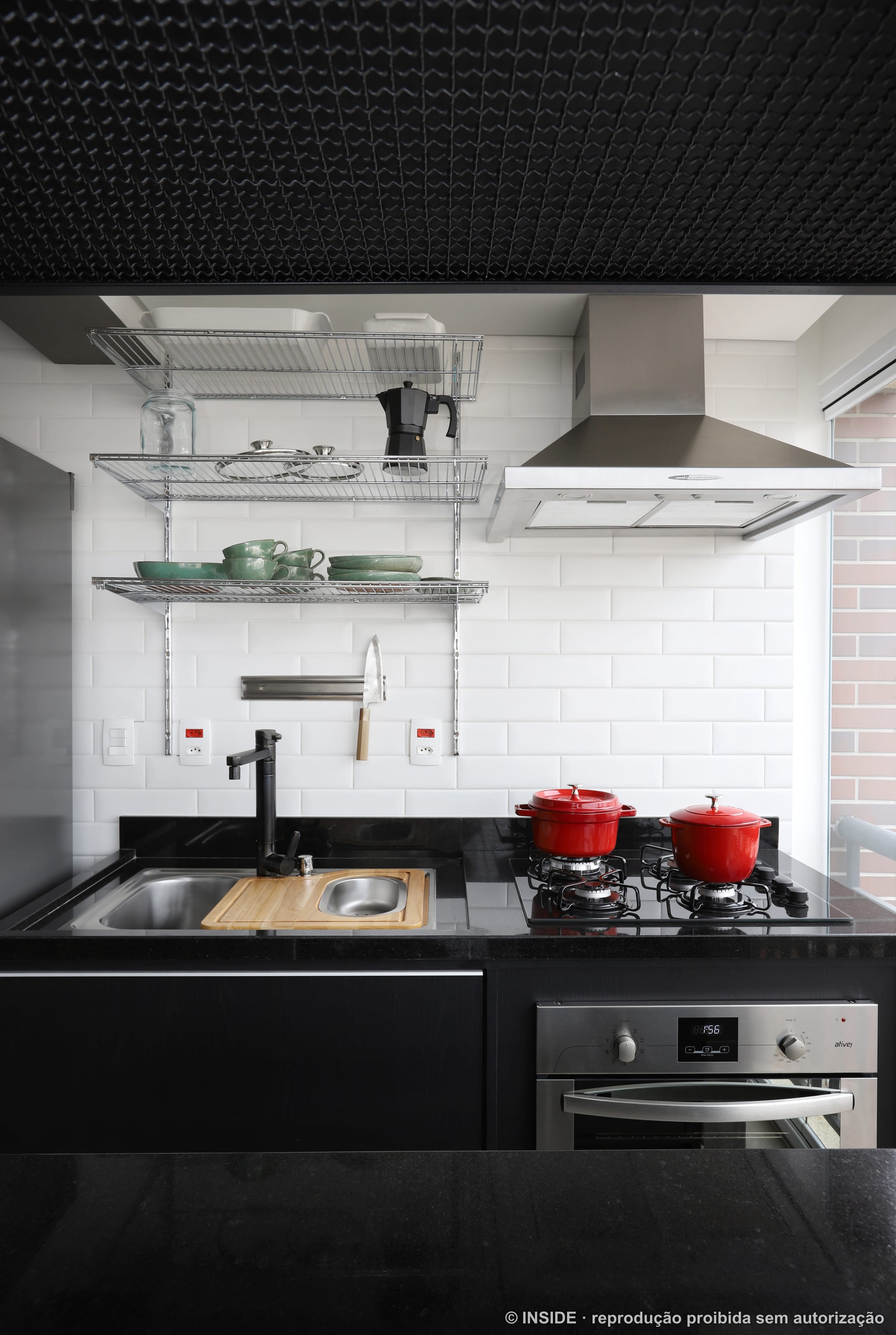 Cozinha industrial com azulejo de metrô branco, prateleira de panelas suspensas e bancada preta, projeto INSIDE