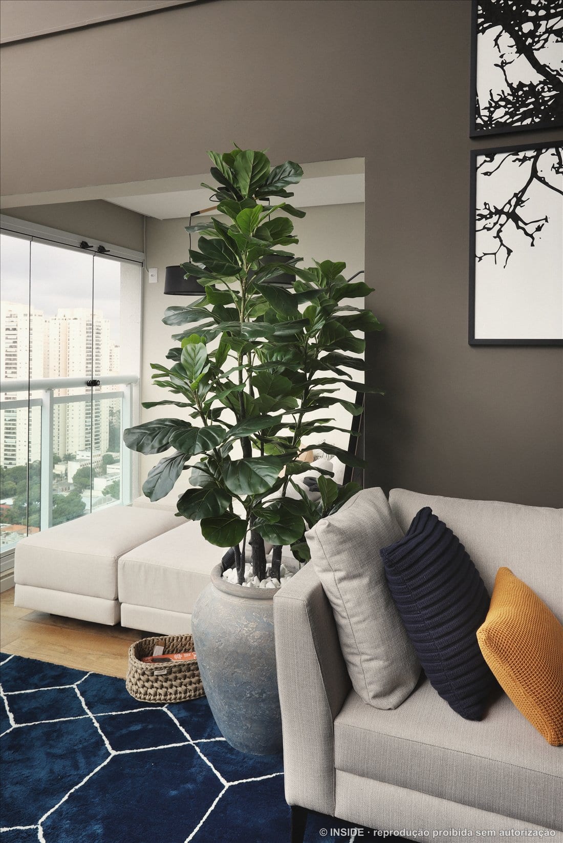 Sala de estar de Priscila e Eduardo com ficus, sofá cinza, tapete azul e vista da cidade, Brooklin, acervo INSIDE 2019