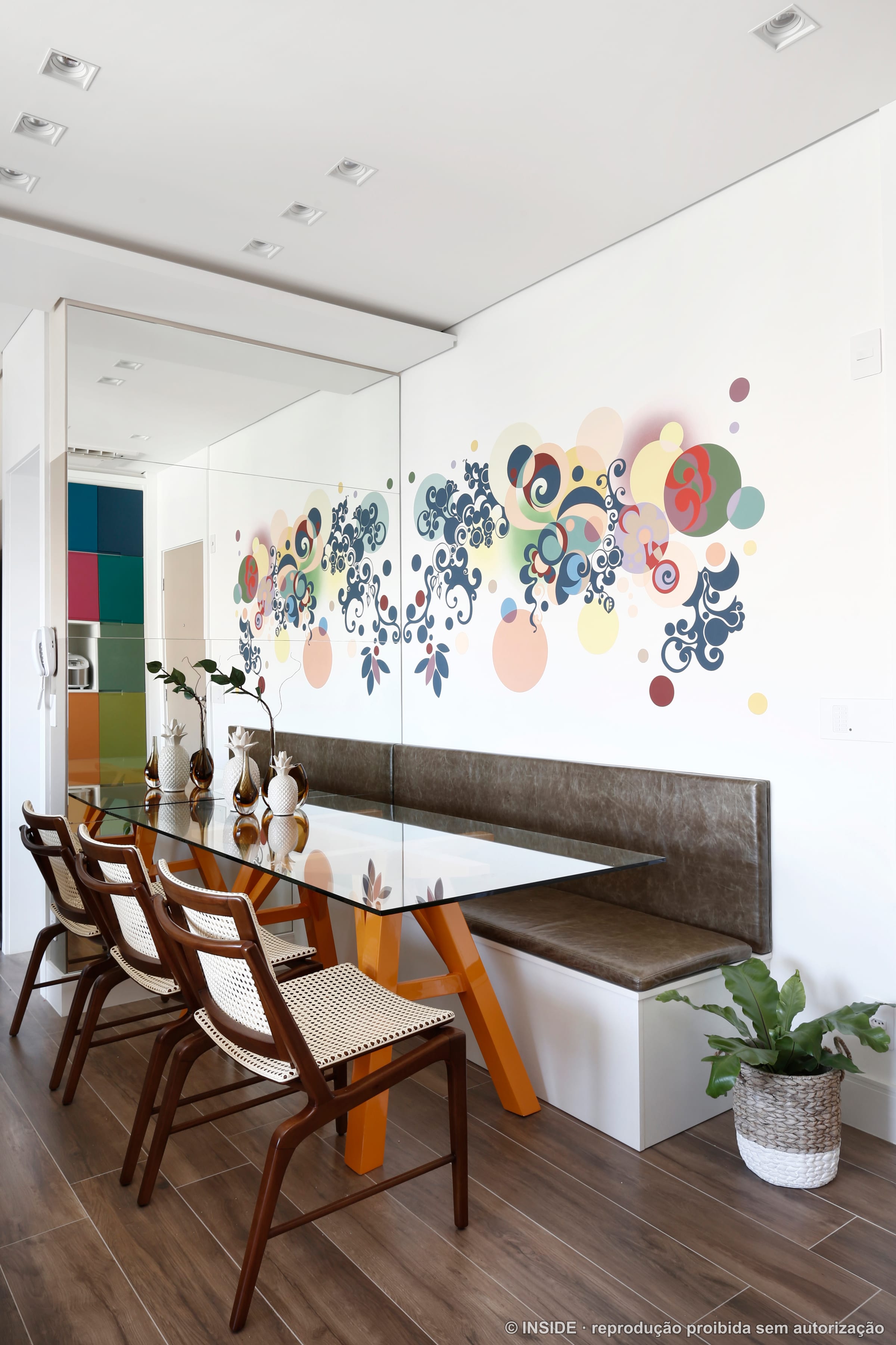 Área de jantar com banco e mural floral colorido na parede, prateleira e plantas, projeto INSIDE