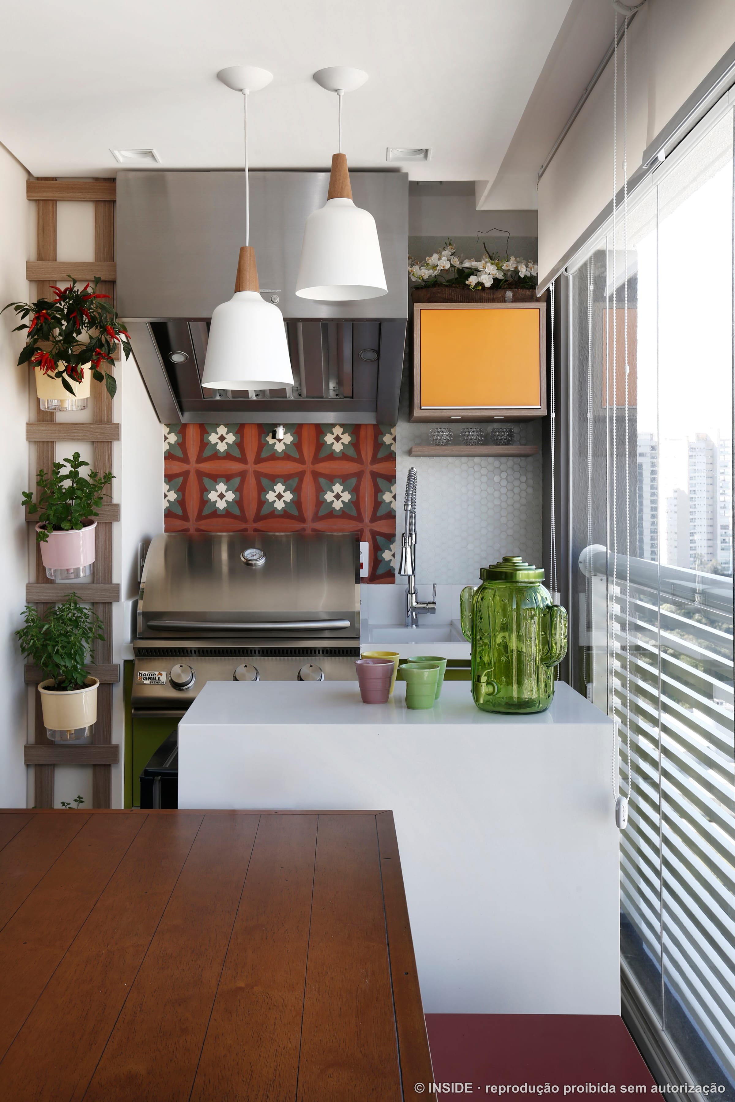 Terraço gourmet com jardineira de plantas, azulejo colorido, bancada e churrasqueira, com a cidade ao fundo, projeto INSIDE