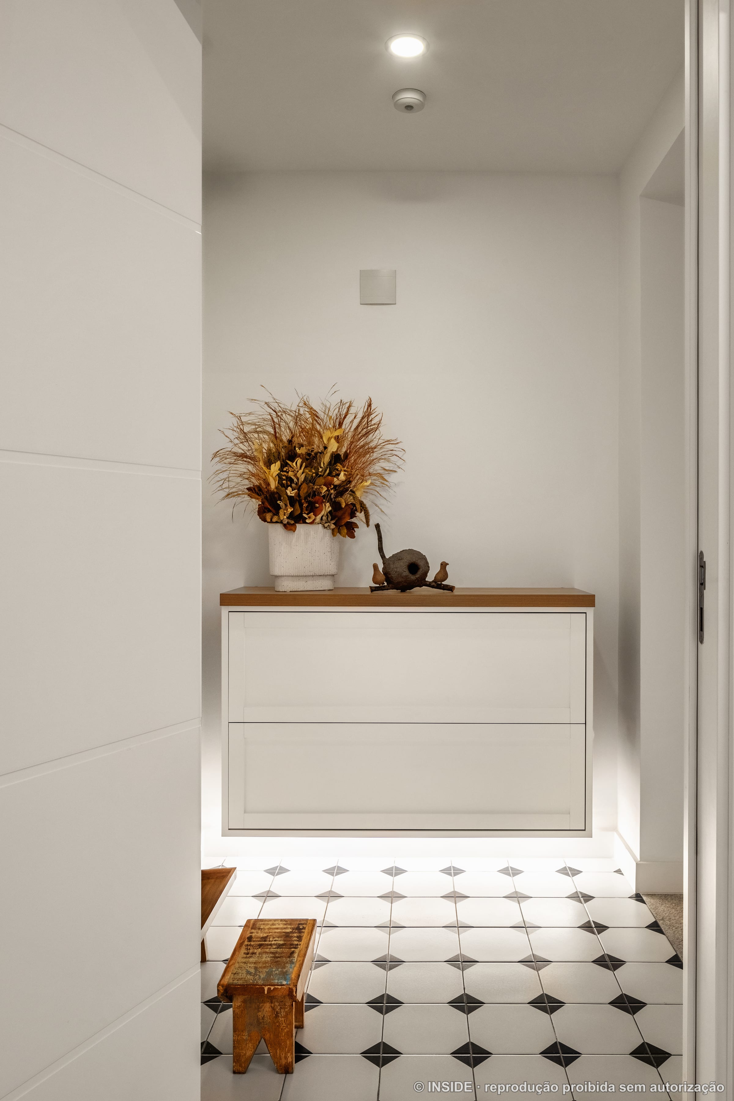 Hall de entrada com aparador suspenso em madeira, vaso de flores secas e piso octogonal preto e branco, projeto INSIDE